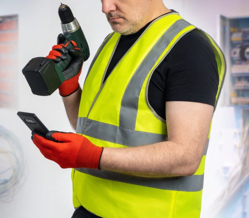 Man repairman with phone. Cropped electrician holds screwdriver. Engineer stands near power panel. Repairman calls customer. Man foreman near electrical equipment. Electrician dressed in yellow vest Man repairman with phone. Cropped electrician holds screwdriver. Engineer stands near power panel. Repairman calls customer. Man foreman near electrical equipment. Electrician dressed in yellow vest
