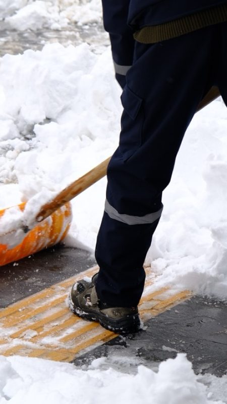 Workers,Sweep,Snow,From,A,City,Road,And,Sidewalk,In Workers sweep snow from a city road and sidewalk in winter. Cleaning city from snow storm