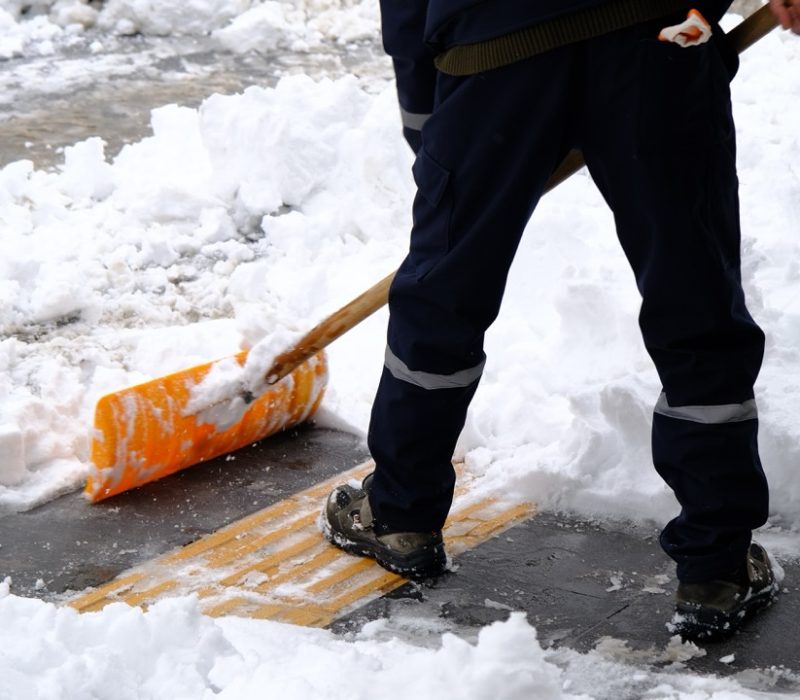 Workers,Sweep,Snow,From,A,City,Road,And,Sidewalk,In Workers sweep snow from a city road and sidewalk in winter. Cleaning city from snow storm